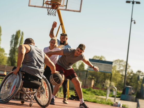 Personne en fauteuil roulant jouant au basket avec son éducateur sportif et d'autres participants lors d'une session de formation CCAIPSH.