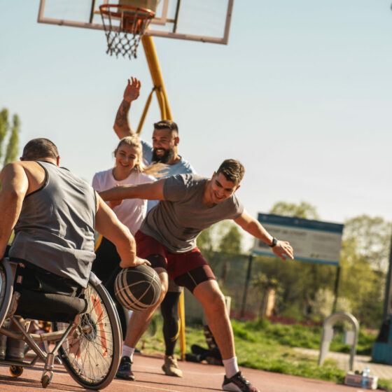 Personne en fauteuil roulant jouant au basket avec son éducateur sportif et d'autres participants lors d'une session de formation CCAIPSH.